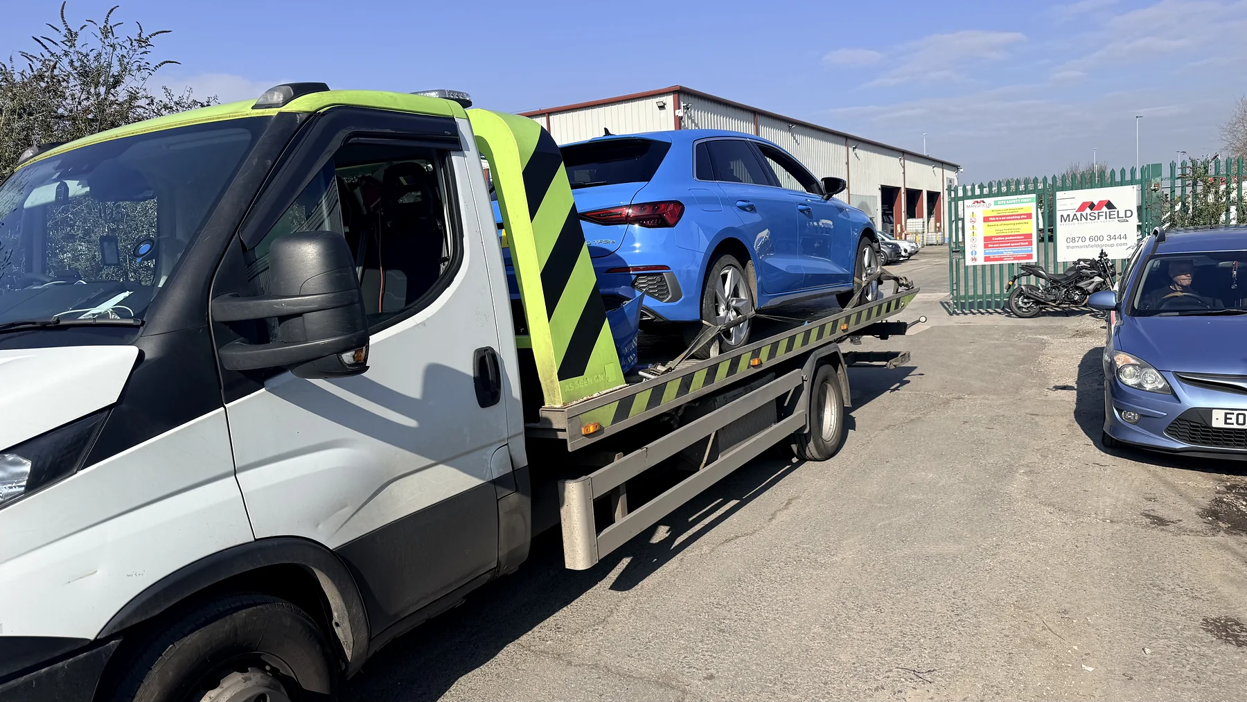 White Iveco recovery truck carrying a blue car