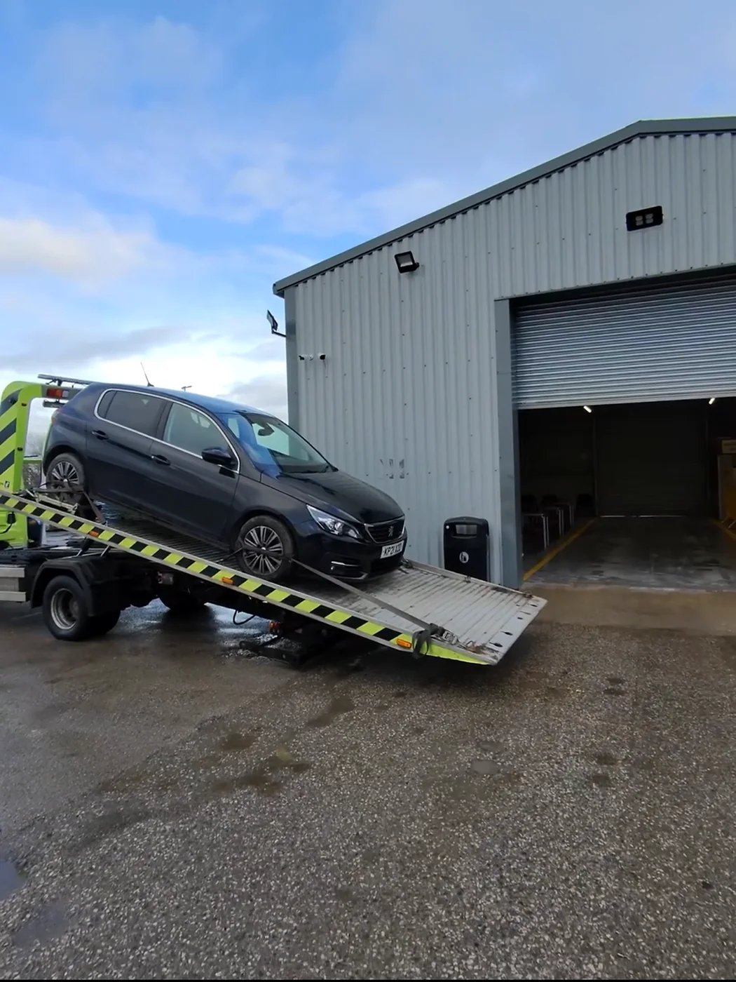 Dark SUV on a lowered recovery bed outside a unit